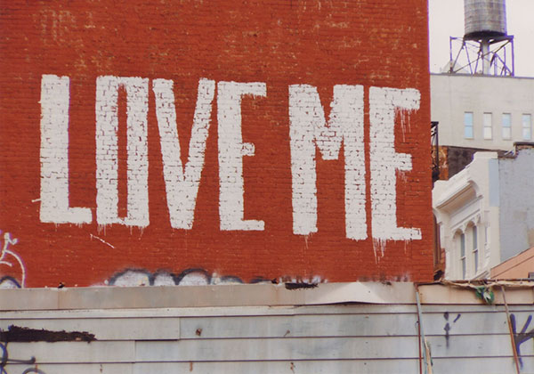 Love Me painted in white text on a red brick wall